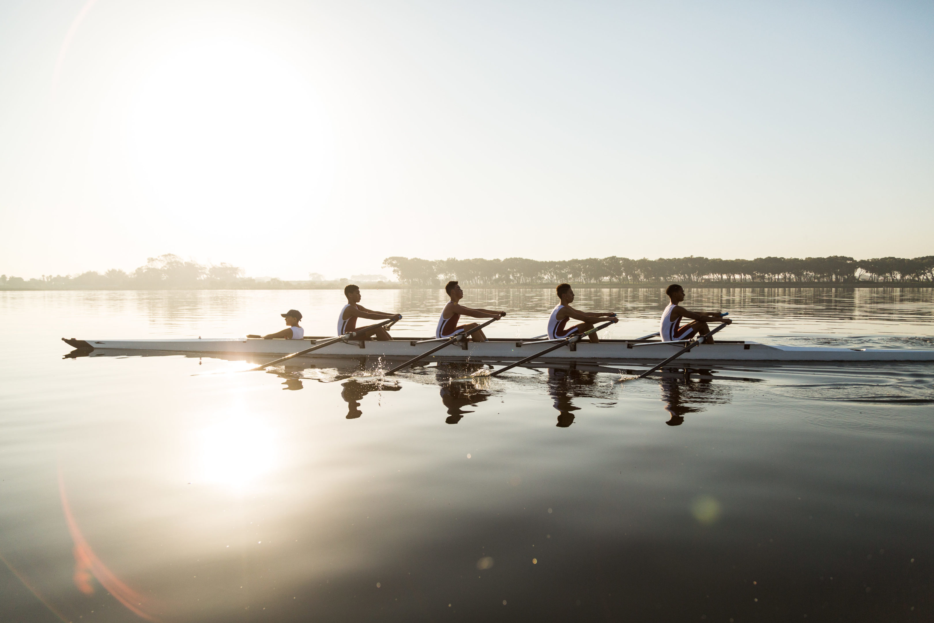 Mixed race rowing team training on a lake at dawn